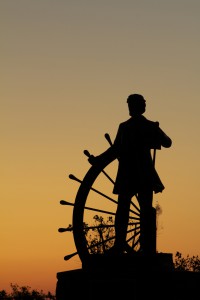 Sunrise silhouette of author Samuel Clemens.   The statue, of Clemens taking the helm of the paddleboat steering. Overlooks the Mississippi River, in Hannibal, Missouri.